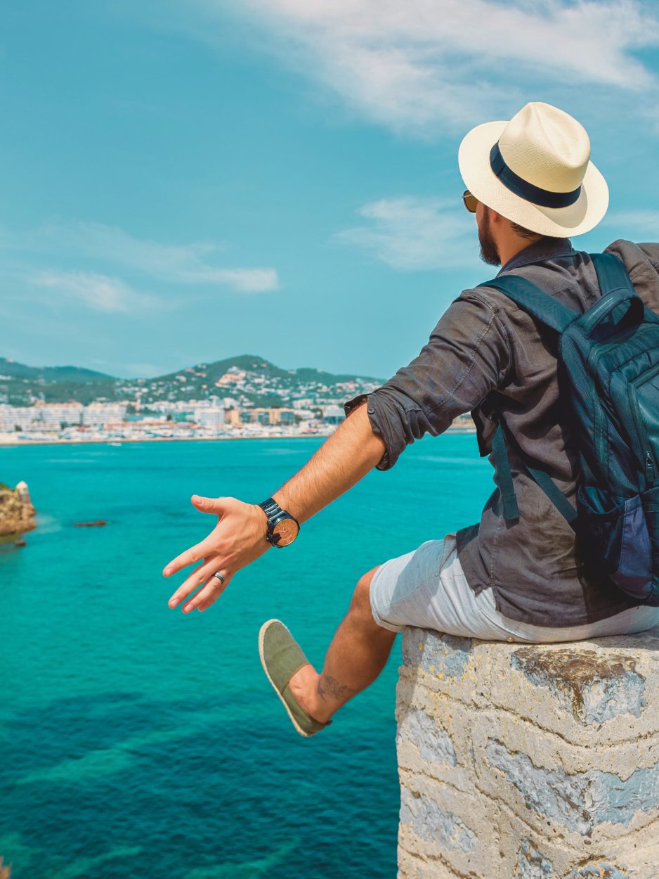 Traveler with a hat and backpack overlooking turquoise water