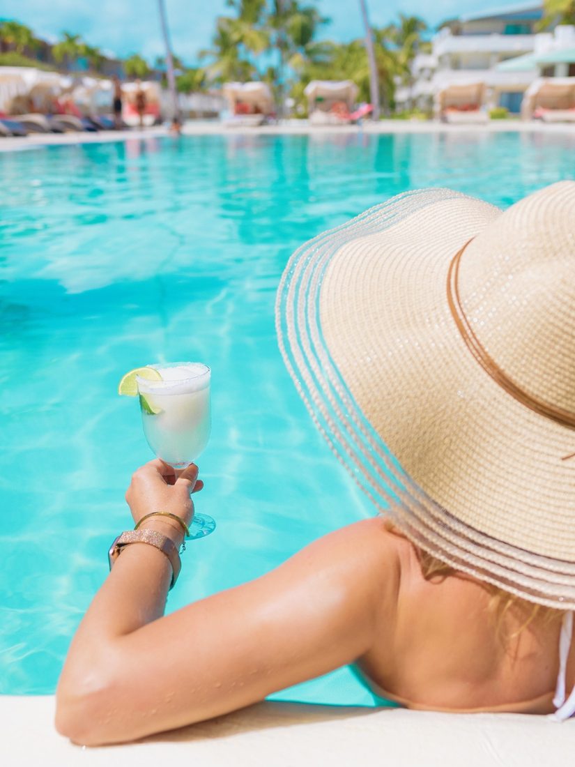 Woman in a sun hat relaxing by a resort pool with a drink